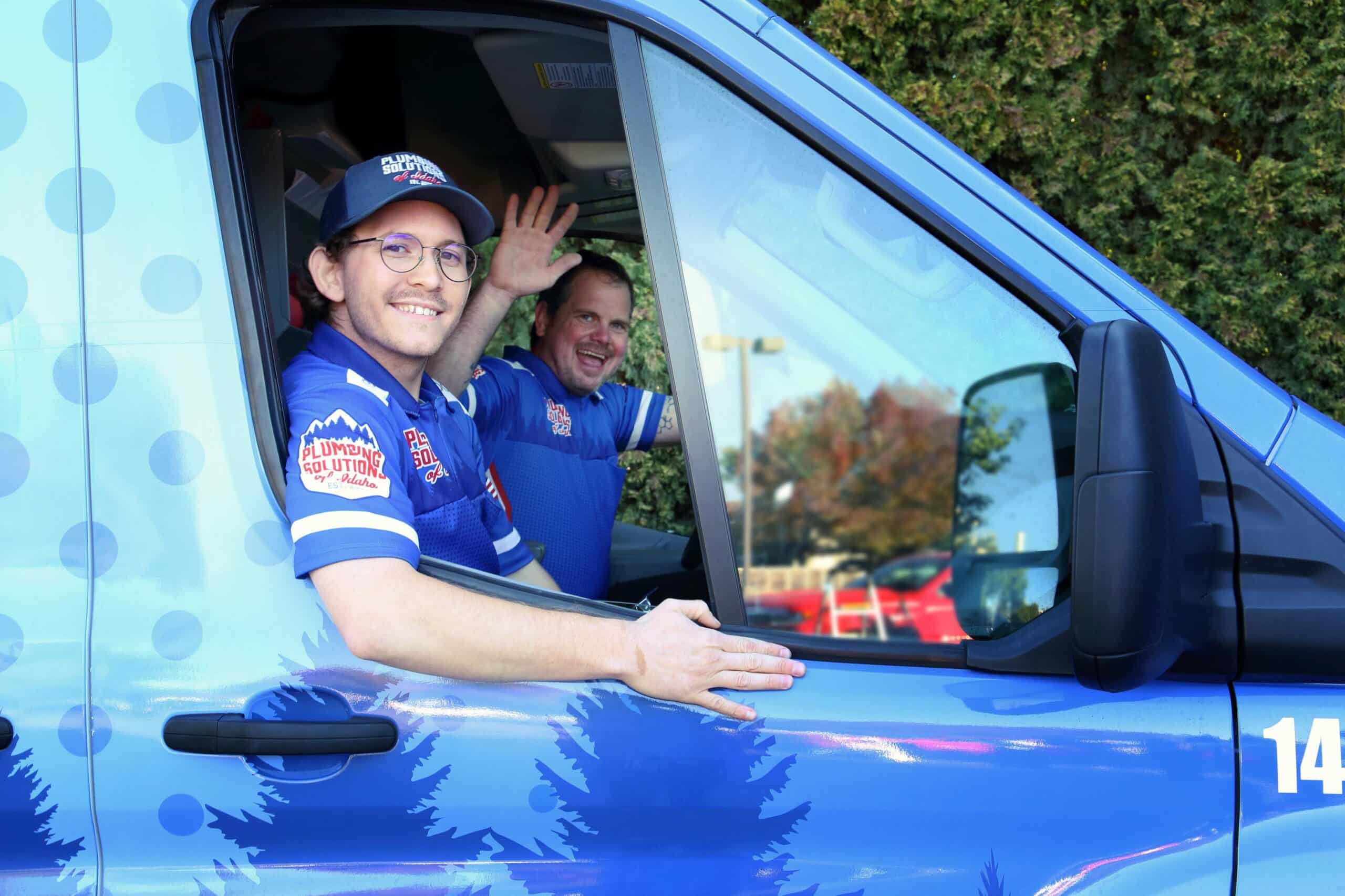 Two employee's waving in plumbing solutions for Idaho work truck