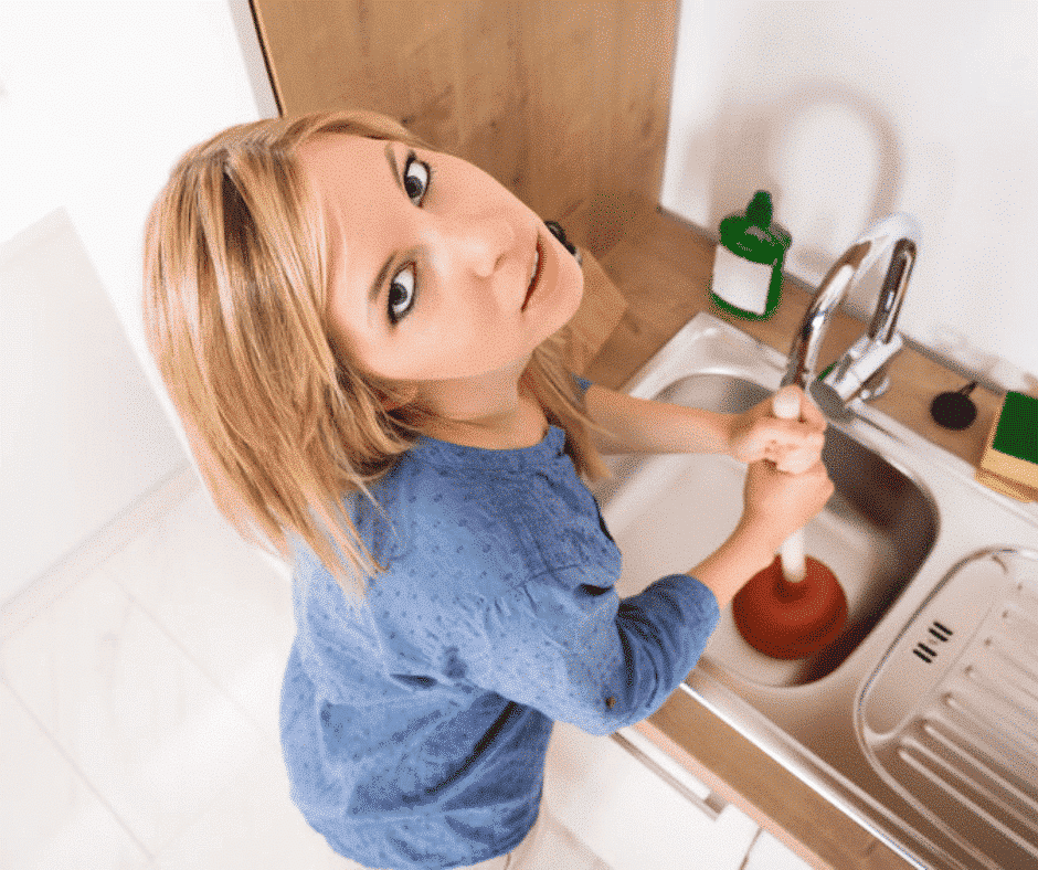 woman using a plunger to get rid of a drain clog in kitchen sink